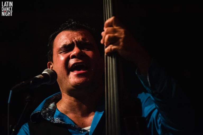 Een man met een microfoon zingt gepassioneerd terwijl hij een contrabas vasthoudt.