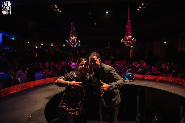 Twee mensen poseren op een podium voor een actief publiek met sfeerverlichting.
