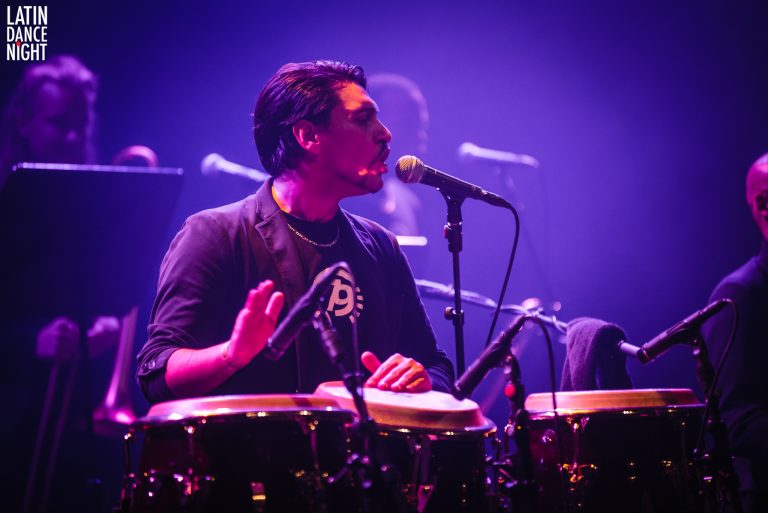 Een muzikant speelt conga's terwijl hij zingt in een levendige, lichtgevende omgeving.