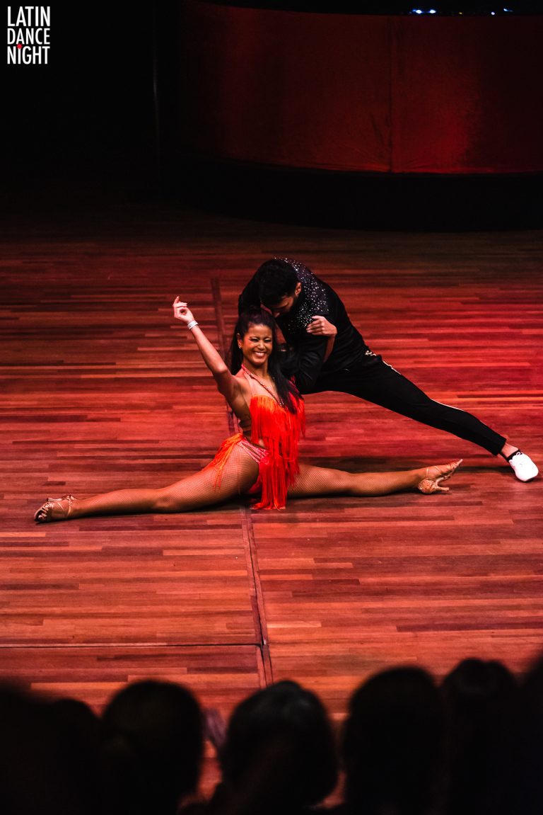 Een danspaar voert een indrukwekkende splits en dansbeweging uit op een houten podium.