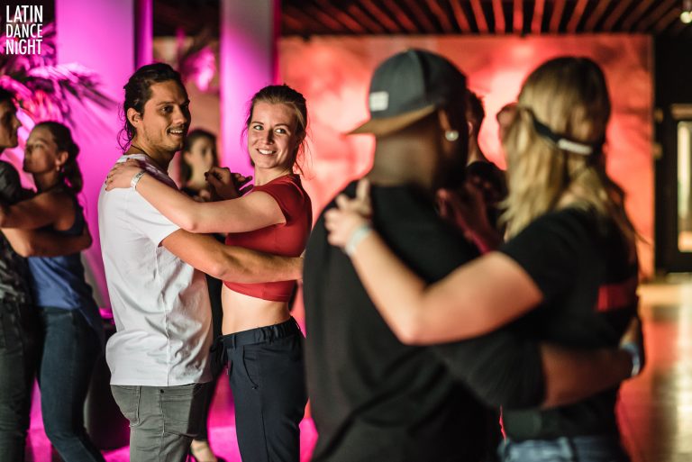 Groep mensen danst samen in een sfeervolle ruimte met kleurrijke verlichting.