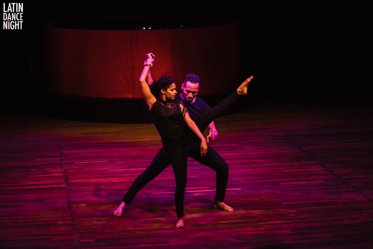 Een danspaar voert een expressieve dansuitvoering uit op een houten vloer met sfeervolle verlichting.