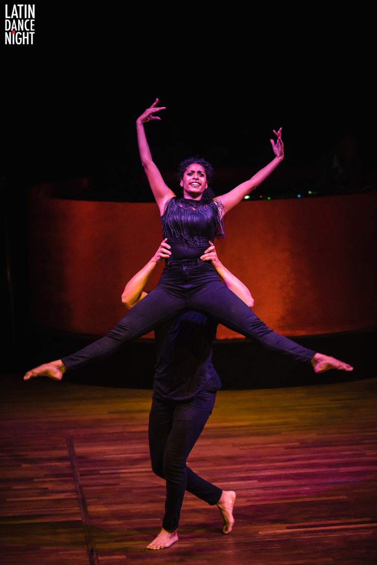Een dansduo voert een complexe move uit, waarbij de vrouwelijke danseres bovenop de mannelijke danser staat met gestrekte armen.