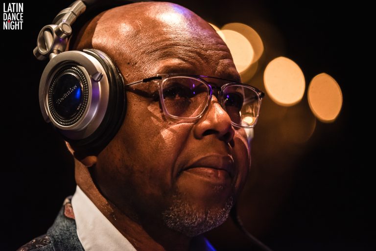 Man met een kaal hoofd en een bril, die naar iets luistert met een hoofdtelefoon op, omringd door een warme, zachte verlichting.