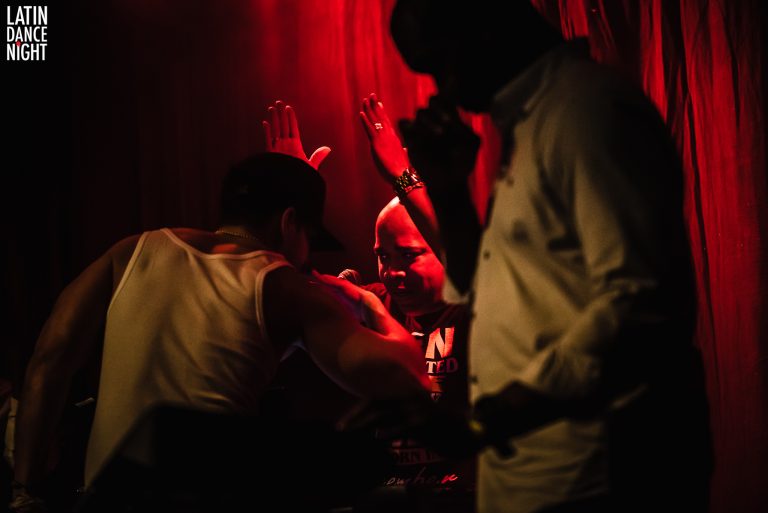 Een intieme muziekscène met silhouetten van artiesten en een warm rood achtergrondlicht.