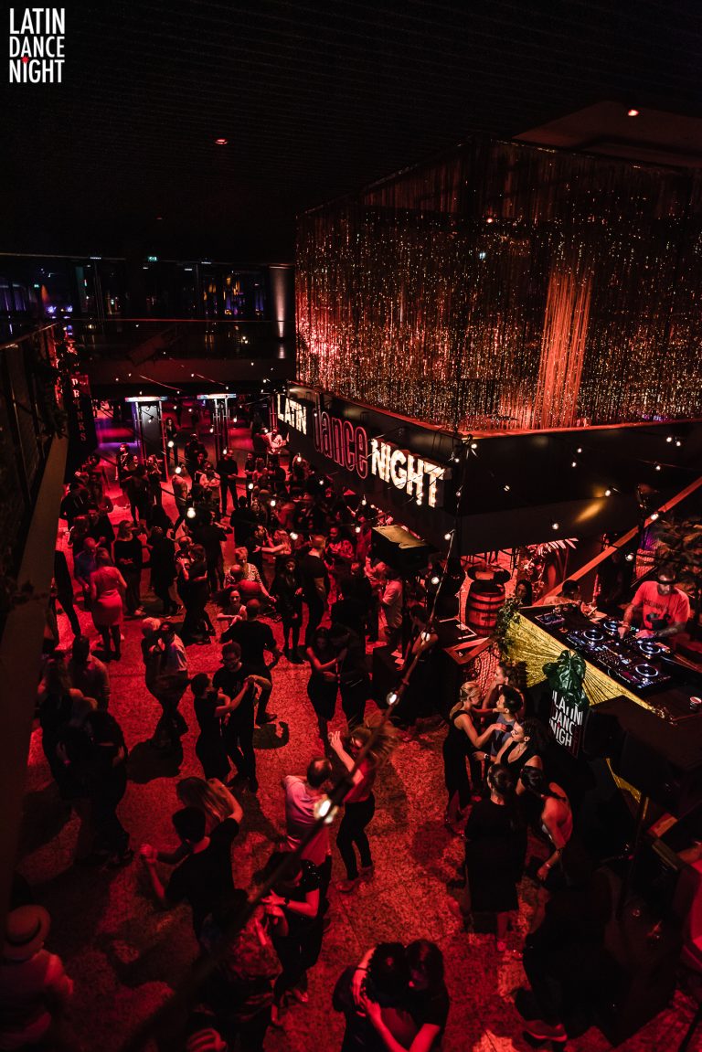 Een drukke nachtclub met felrode verlichting en een DJ aan de draaitafels.