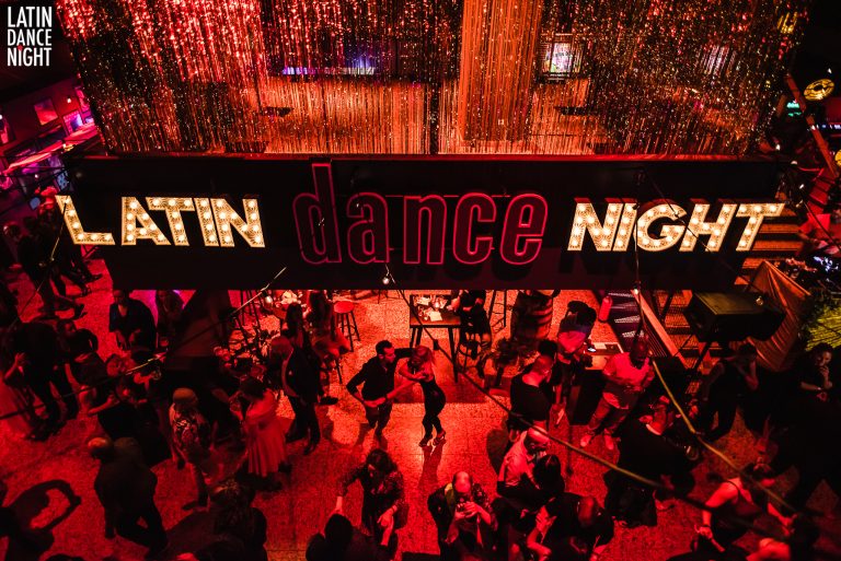 Een levendige dansvloer met mensen die dansen onder een lichtgevend bord met de tekst 