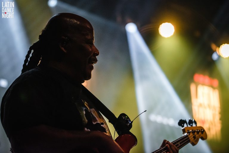 Silhouet van een muzikant die op een elektrische gitaar speelt, verlicht door kleurrijke stageverlichting.