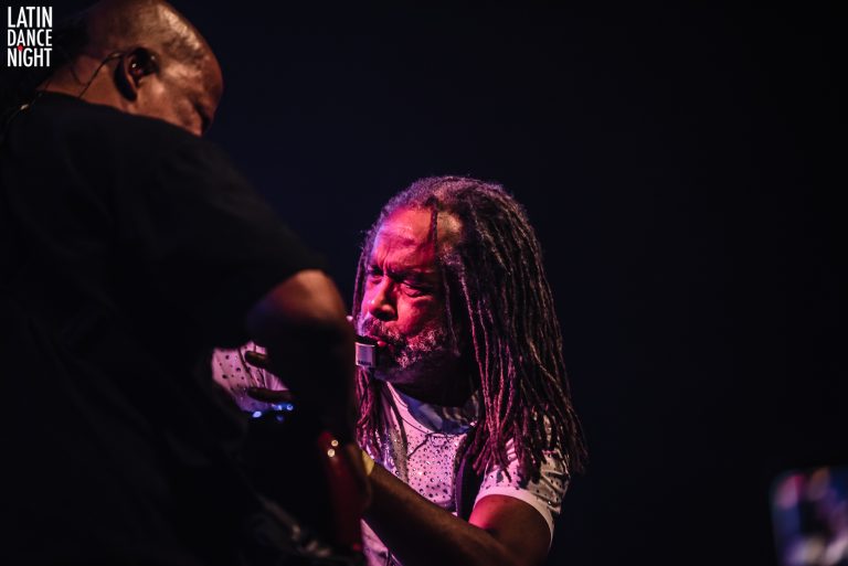 Twee muzikanten spelen samen op een podium in een low-light omgeving.