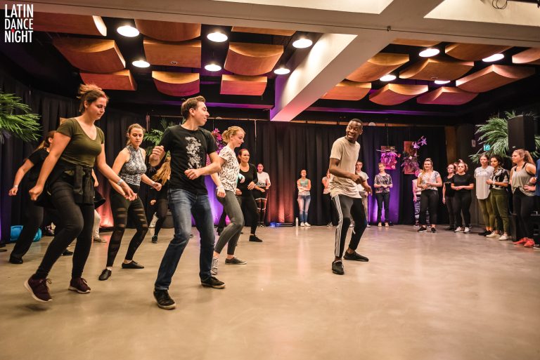 Groep mensen danst samen in een studio met kleurrijke verlichting.