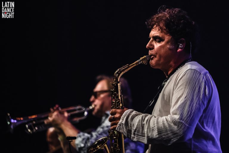 Twee muzikanten spelen op een podium, waarvan een man een saxofon bespeelt.