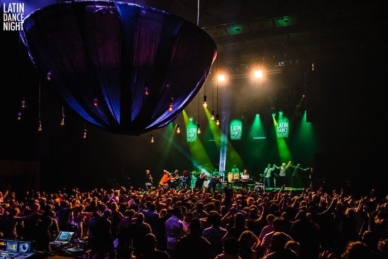 Een drukke concertbeleving met een enthousiast publiek en kleurrijke verlichting.