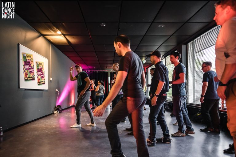 Een groep mannen danst in een moderne ruimte met sfeerverlichting.