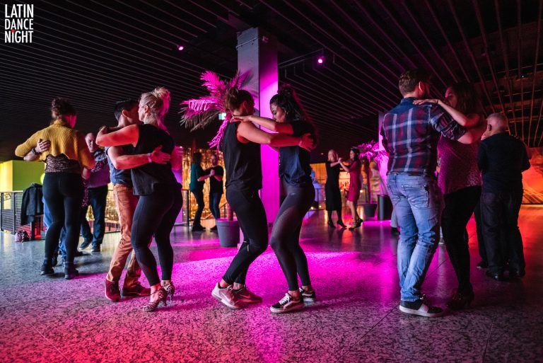 Groep mensen danst samen onder kleurrijke verlichting in een moderne omgeving.