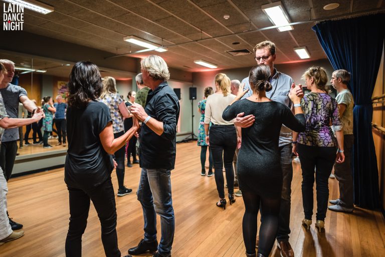Een dansles met verschillende mensen die in groepjes aan het dansen zijn in een zaal.
