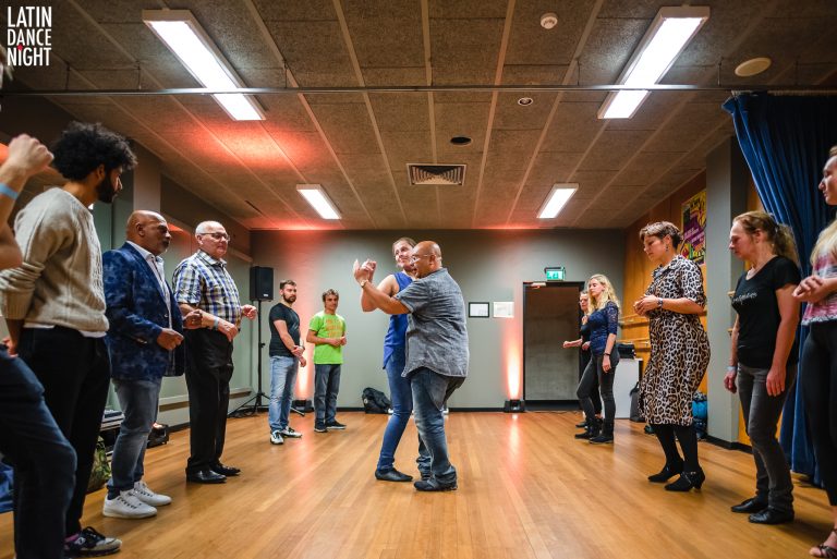 Een groep mensen danst samen in een zaal met houten vloeren en sfeervolle verlichting.