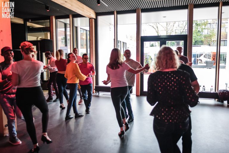 Groep mensen danst samen in een moderne ruimte met grote ramen.