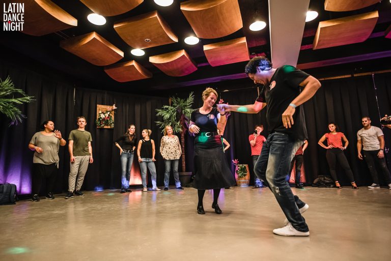 Mensen dansen samen in een ruimte met kleurrijke verlichting en een gezellige sfeer.