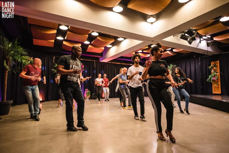 Groep mensen danst in een studio met sfeerverlichting en een moderne inrichting.