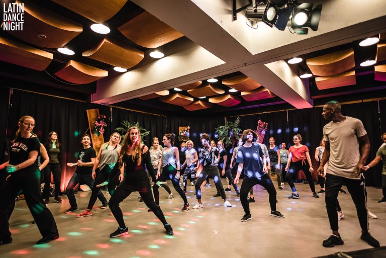 Group of people participating in a lively dance class with colorful lights in a studio.