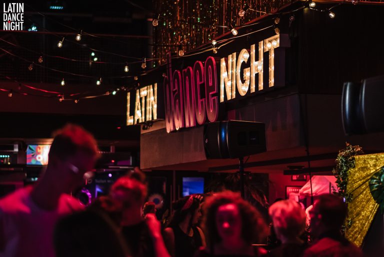 Een drukke dansvloer met een oplichtend bord dat 