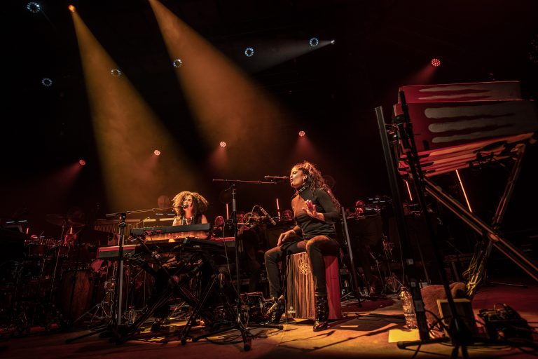 Twee muzikanten spelen live op een podium, verlicht door warmespots.