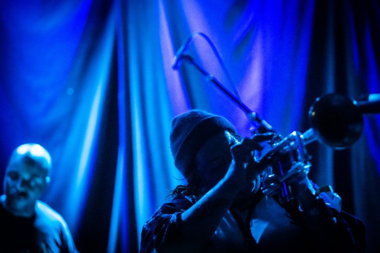 Een silhouet van een muzikant die op een trompet speelt, met een blauwe achtergrondverlichting.