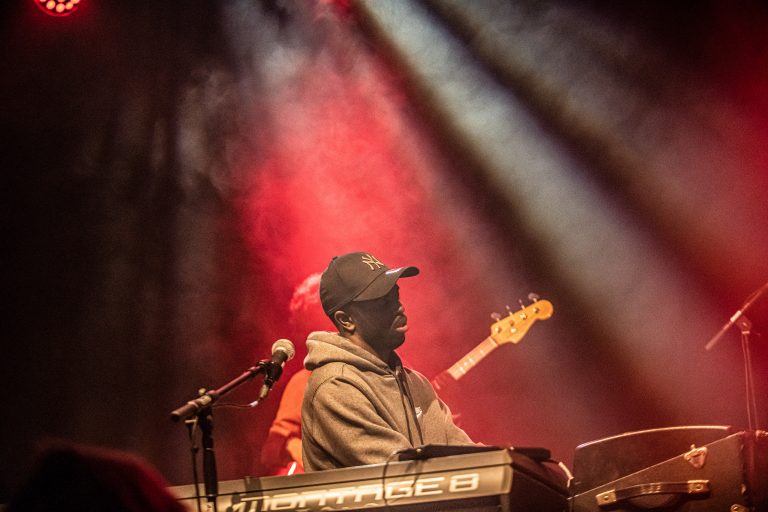 Een muzikant speelt op een keyboard onder kleurrijke lichten tijdens een live optreden.