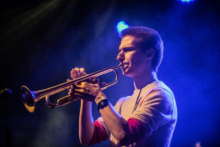 Een muzikant speelt op een trompet onder kleurrijke stageverlichting.