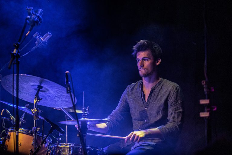 Een drummer speelt in een sfeervolle, blauwe lichtsetting.