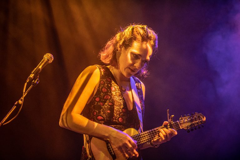 Een vrouwelijke muzikant speelt een ukulele op het podium onder kleurrijke verlichting.