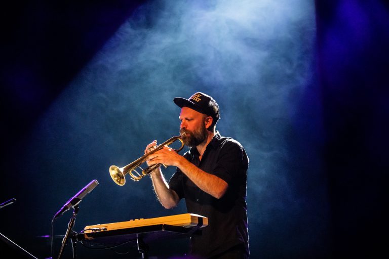 Een muzikant speelt trompet onder een blauwe lichtshow.