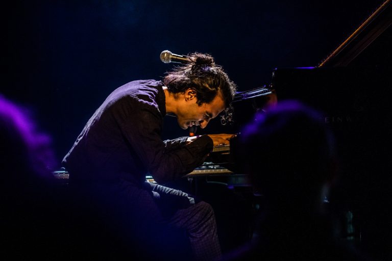 Een muzikant speelt intensief pianomuziek op een donkere Bühne.