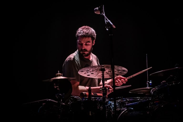 Een drummer speelt enthousiast op zijn drums in een donkere omgeving.