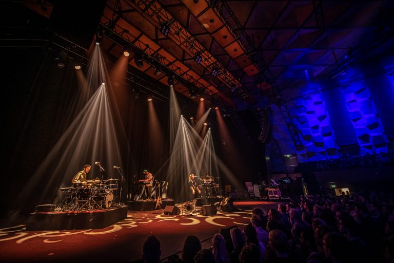 Een live muziekevenement met bandleden op het podium en theatrale verlichting.