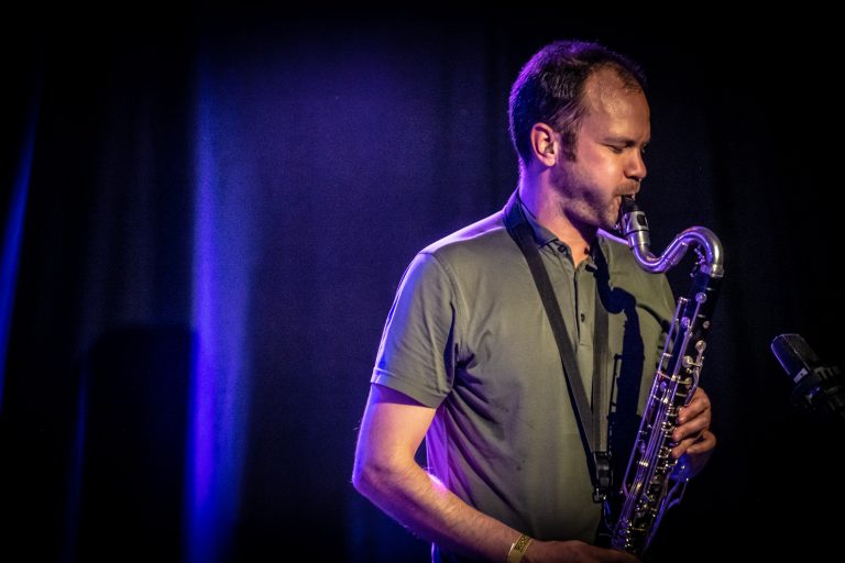 Een muzikant speelt op een saxofoon onder een zachte, paarse verlichting.