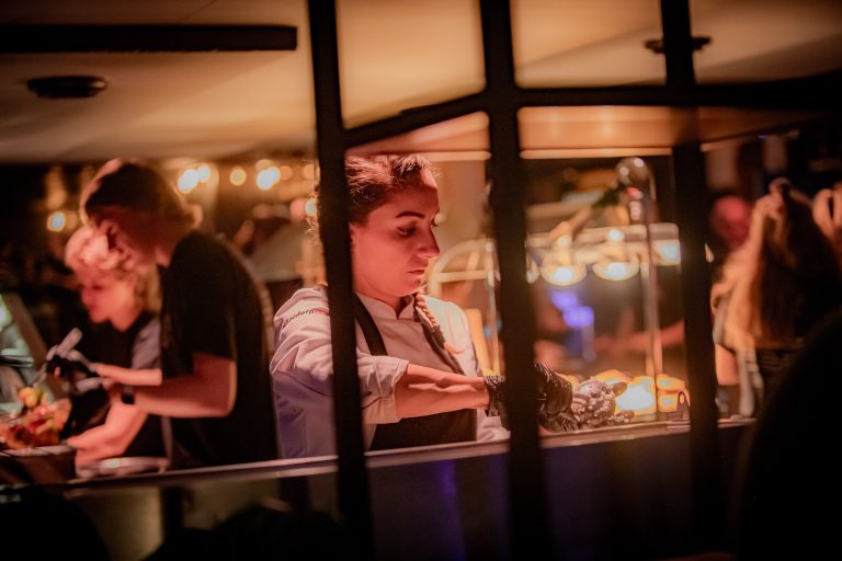 Een vrouwelijke chef-kok werkt achter een eetstand, omgeven door sfeervolle verlichting.