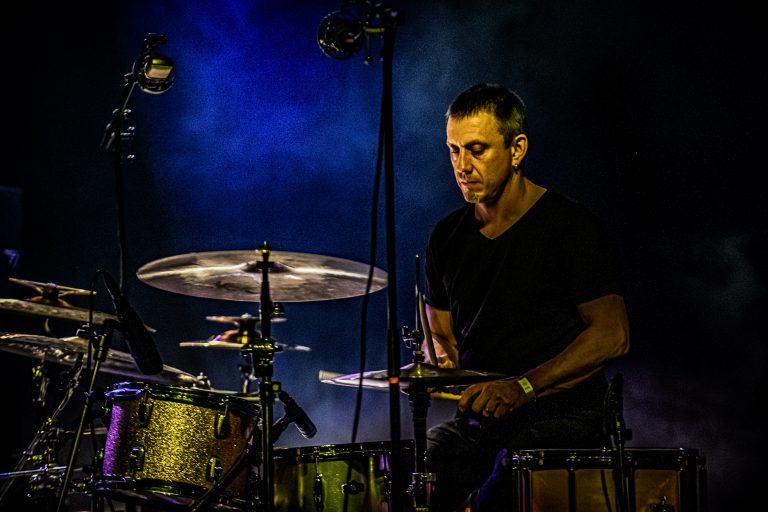 Een drummer speelt op een podium met blauwe verlichting.