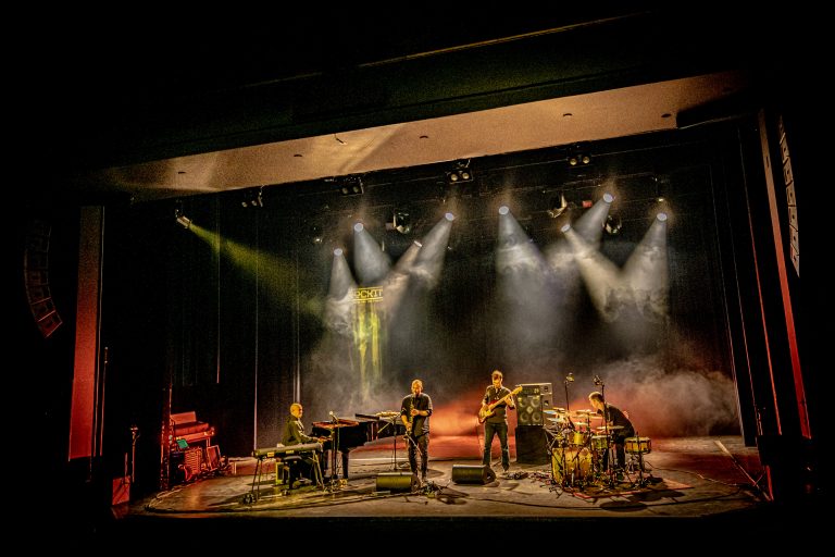 Een muziekband performt live op een podium met kleurrijke verlichting.