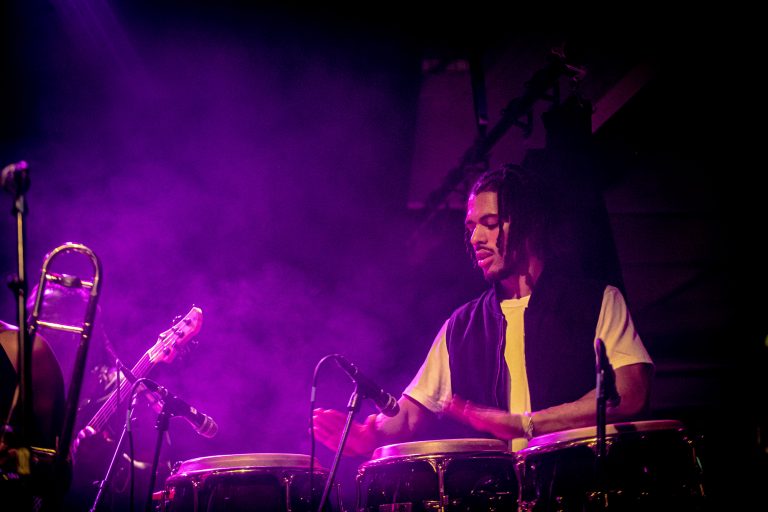 Een muzikant speelt op conga's in een sfeervolle, paarse verlichting.