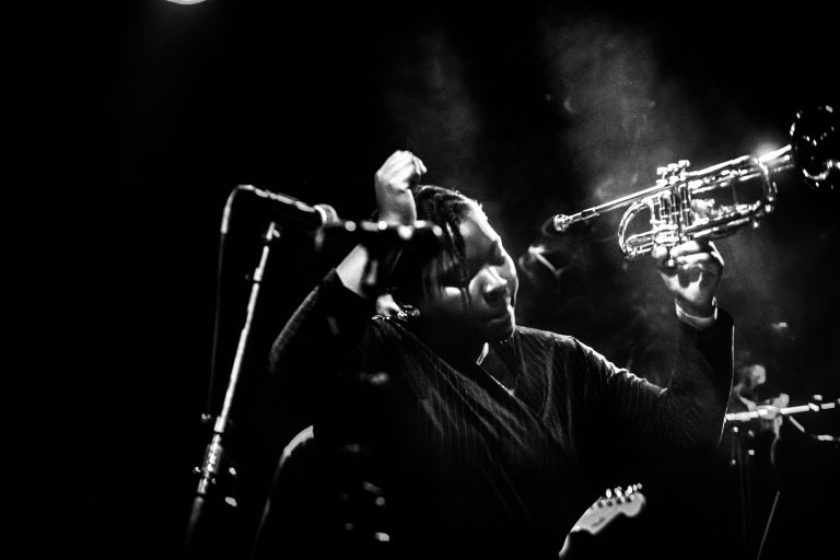 Een muzikant die een trompet speelt tijdens een live optreden in zwart-wit.