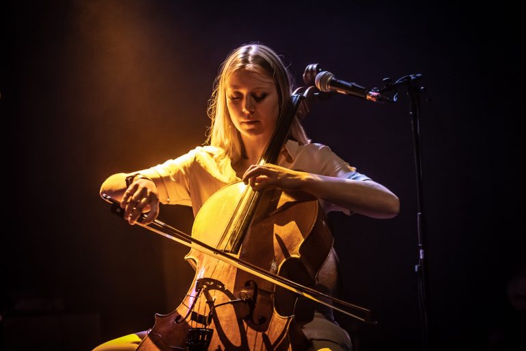 Een vrouwelijke muzikant speelt een cello op het podium, verlicht door warme lichteffecten.