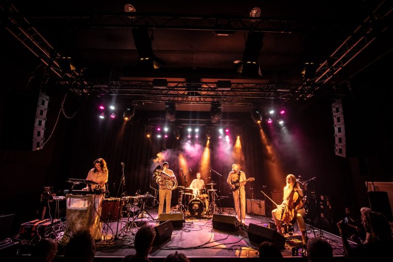 Een band speelt live op een podium met kleurrijke lichten.