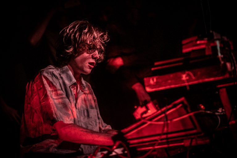 Een muzikant speelt op een keyboard in een sfeer met rode verlichting.