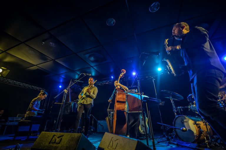 Een jazzband speelt op een podium met blauwe verlichting.