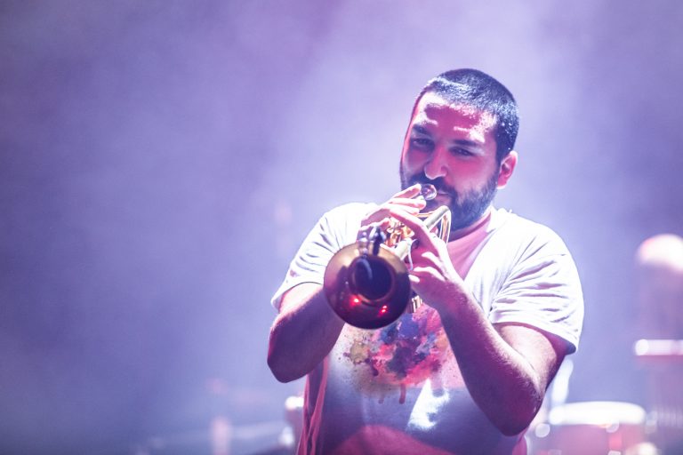 Een man speelt een trompet op een podium met kleurrijke verlichting.