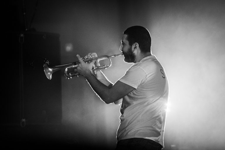 Een man speelt trompet op het podium in een zwakke verlichte omgeving.