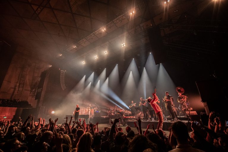 Een energiek concert met een levendig publiek en opvallende lichten die het podium verlichten.