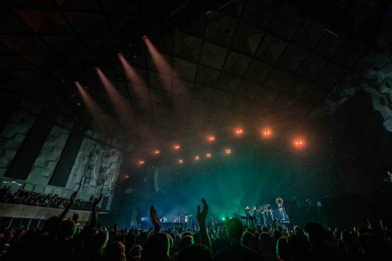 Een live concert met enthousiaste fans en kleurrijke lichten op het podium.