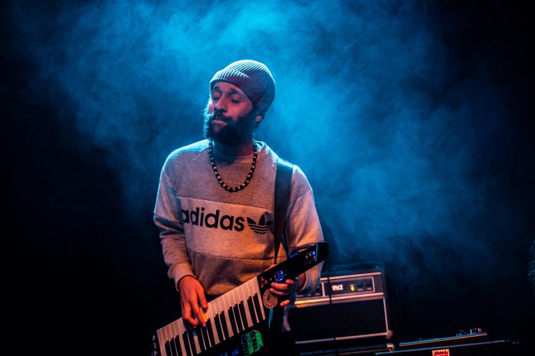 Een muzikant speelt op een elektrisch keyboard onder een blauwe belichting met rookeffect.